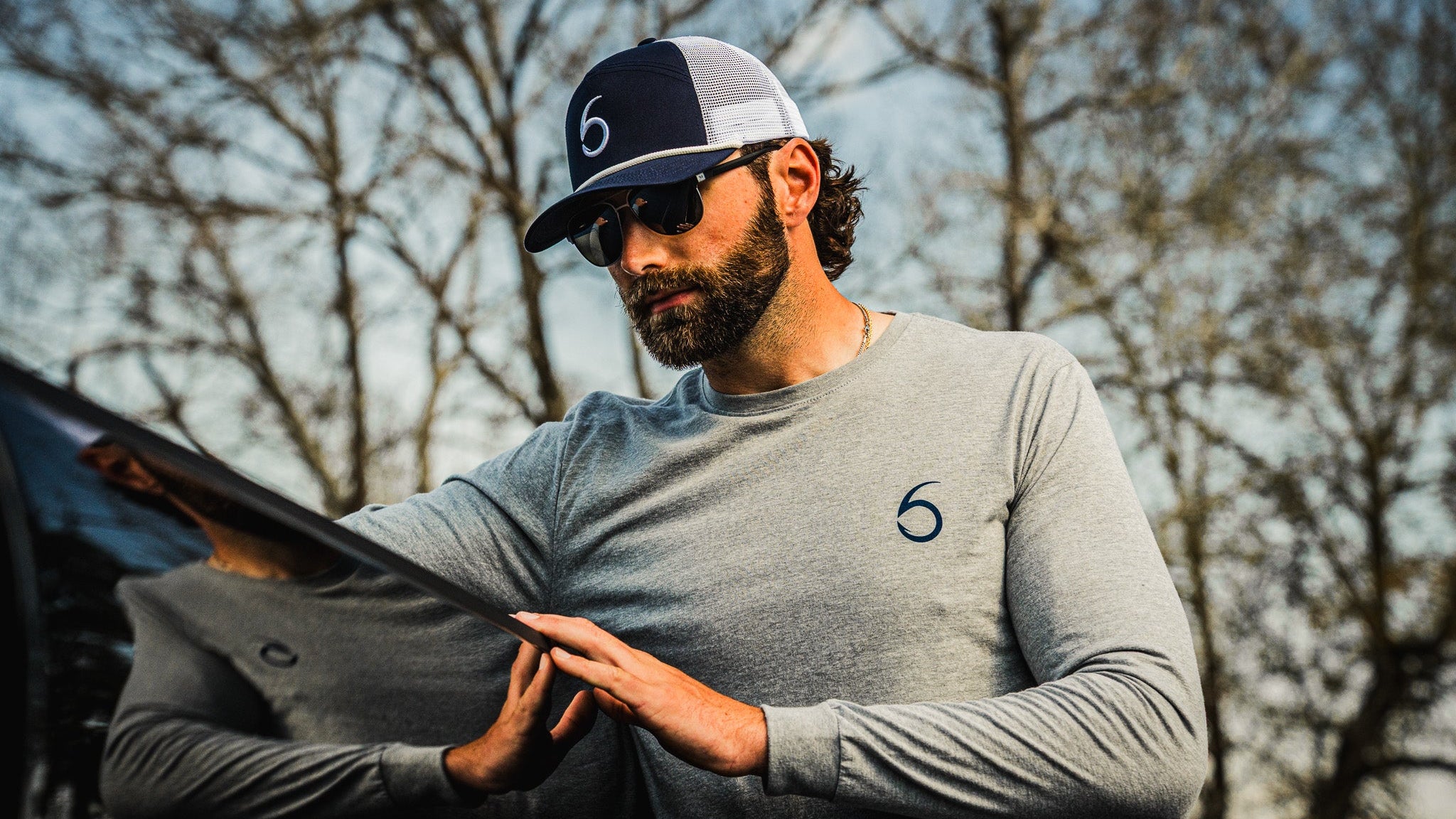 Man wearing a gray long-sleeve shirt with a logo, holding a jacket outdoors.